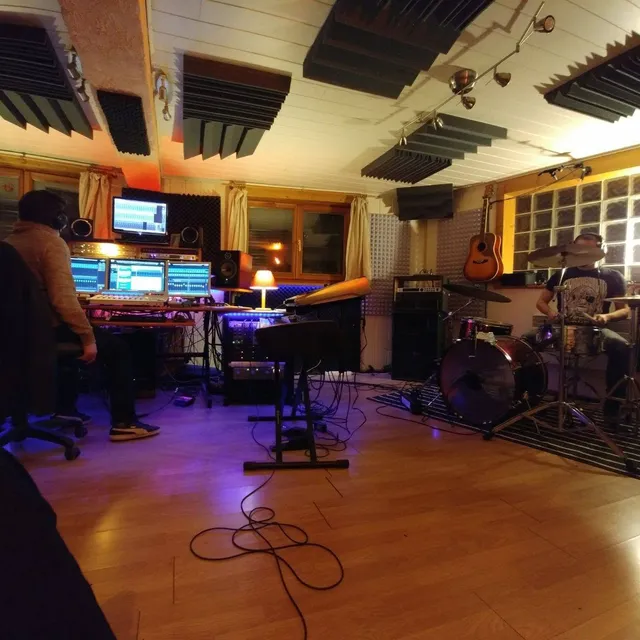 Session d'enregistrement dans la control room : ingénieur du son aux écrans, batteur en train de jouer